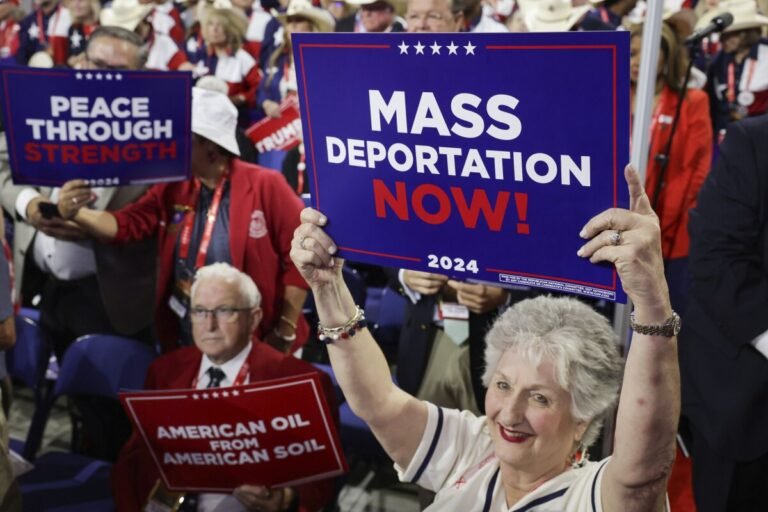 People hold signs that read "Mass Deportation Now!" on the third day of the Republican National Convention.