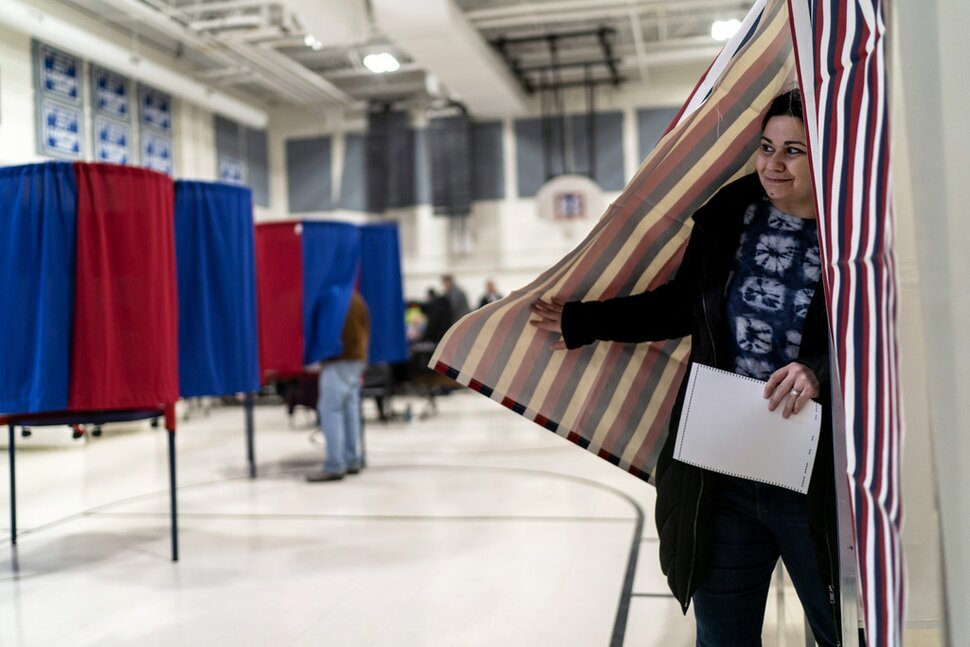 A woman emerges from a voting booth after filling out her ballot for the New Hampshire presidential primary at a polling site, Jan. 23, 2024, in Manchester, N.H.